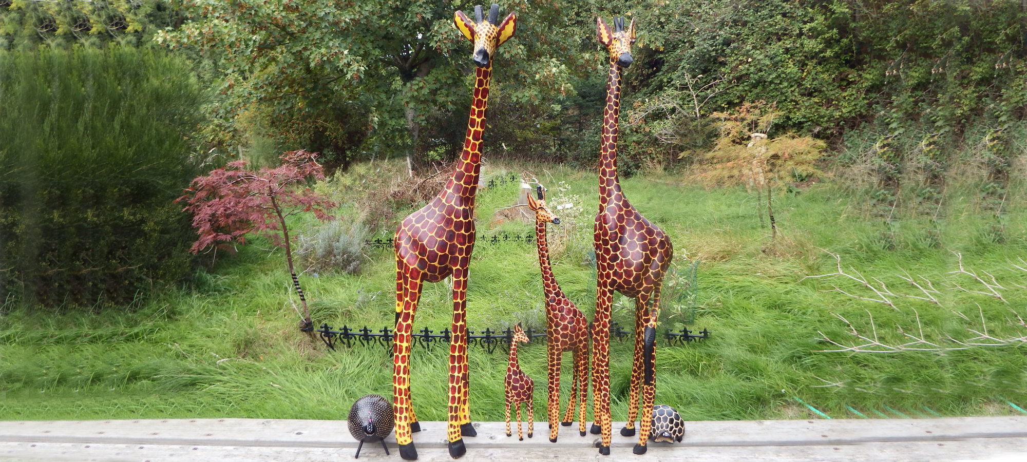 Two hand-carved wooden giraffes, painted in warm browns and yellows, standing outdoors in Kenya